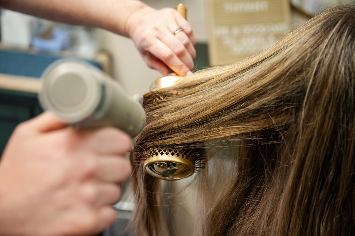 Close up photo of a hairstylist blowdrying her clients hair in her salon in Plano, TX.