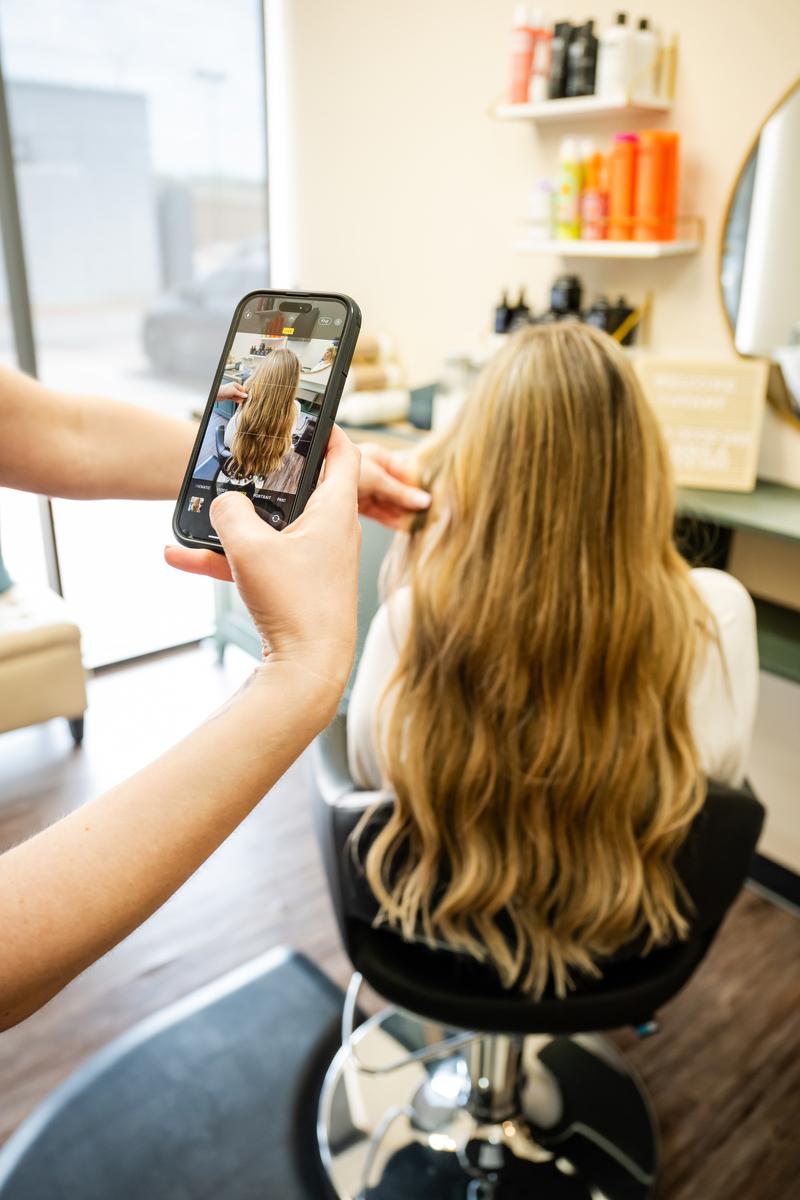 Hairstylist taking an after photo of her hair extension client at her salon in Plano, TX.